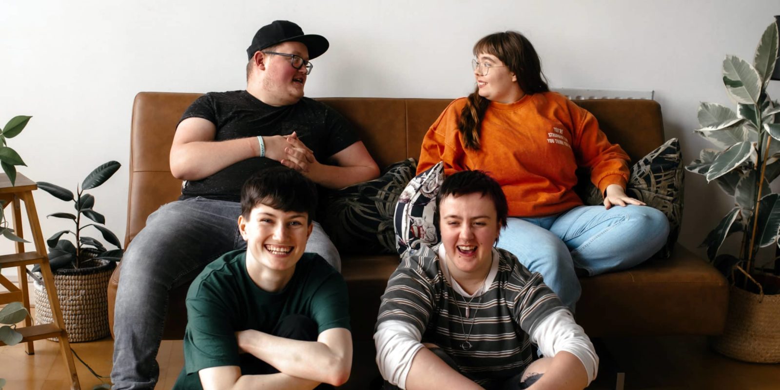 Group of young people laughing together, two sat on floor, two sat on sofa