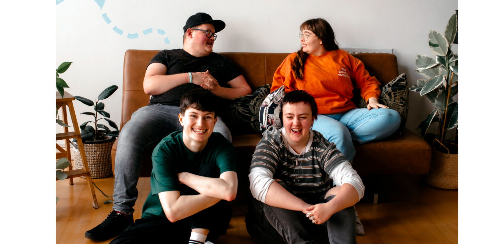 Group of young people laughing together, two sat on floor, two sat on sofa