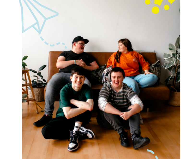 Group of young people laughing together, two sat on floor, two sat on sofa