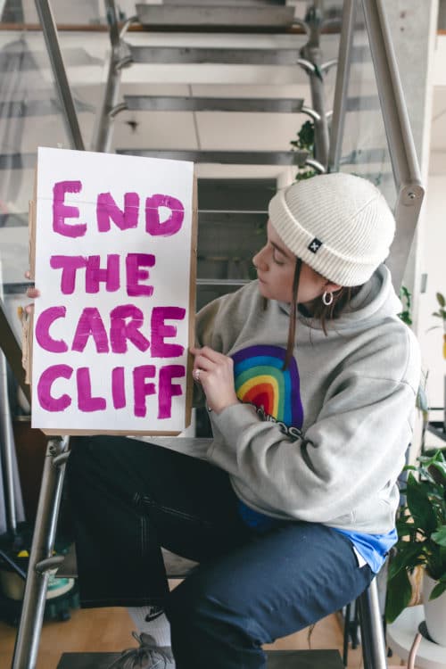 Beth looking at end the care cliff sign sat on the stairs