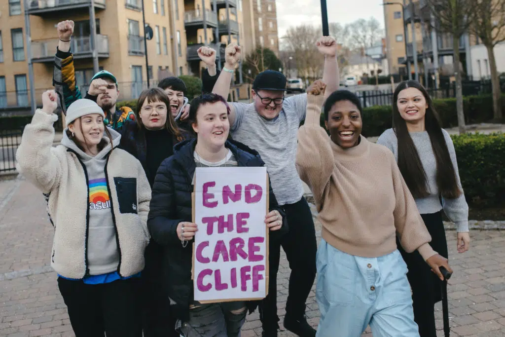 Group of young people with raised fists and end the care cliff sign