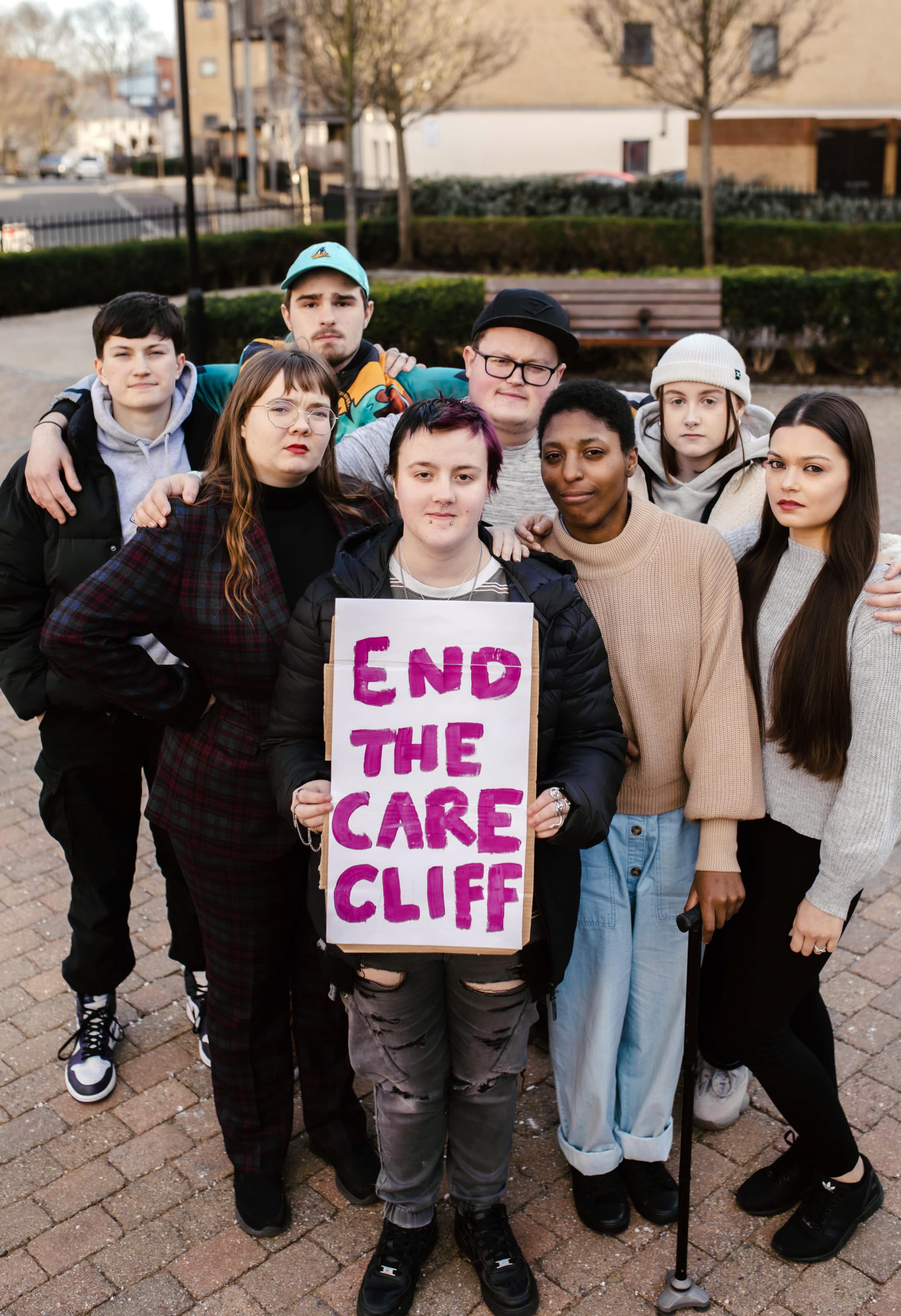 Group of young people looking into camera with arms around holding a sign that reads end the care cliff