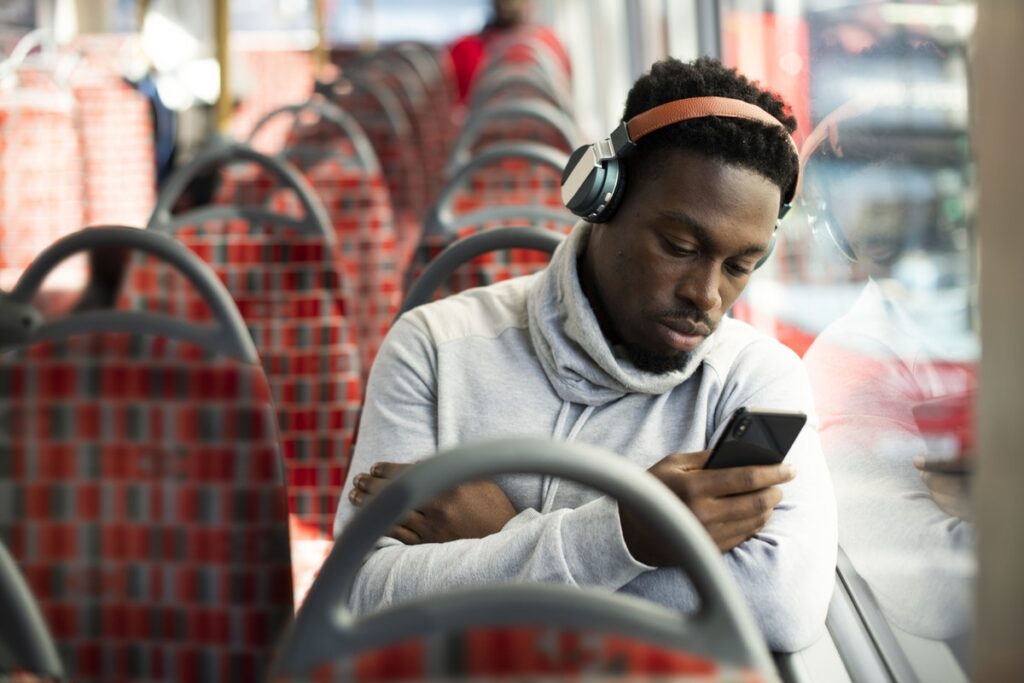 Young man on a bus wearing headphones and looking at a phone