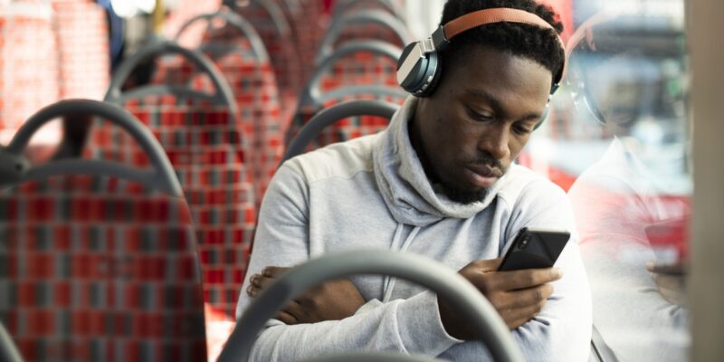 Young man on a bus wearing headphones and looking at a phone