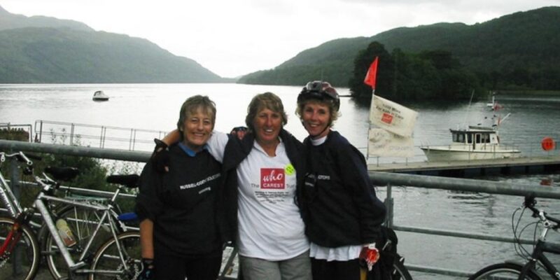 Pip, Gill and a friend stand in front of a lake with their bikes