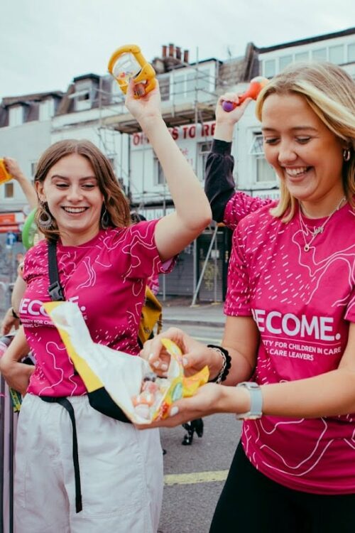 Three women in pink Become tops. One of them is holding an open packet of sweets
