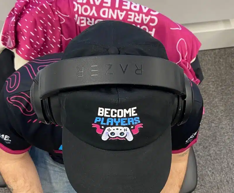 Someone sitting down wearing a Become Players cap