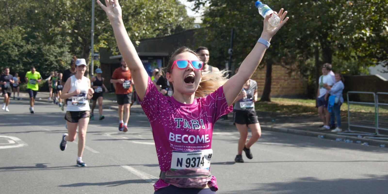 Woman in pink top smiling whilst running with arms in the air