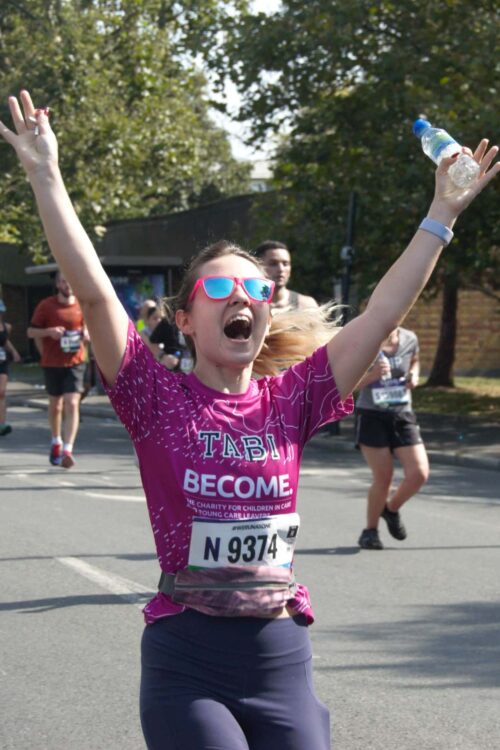 Woman in pink top smiling whilst running with arms in the air