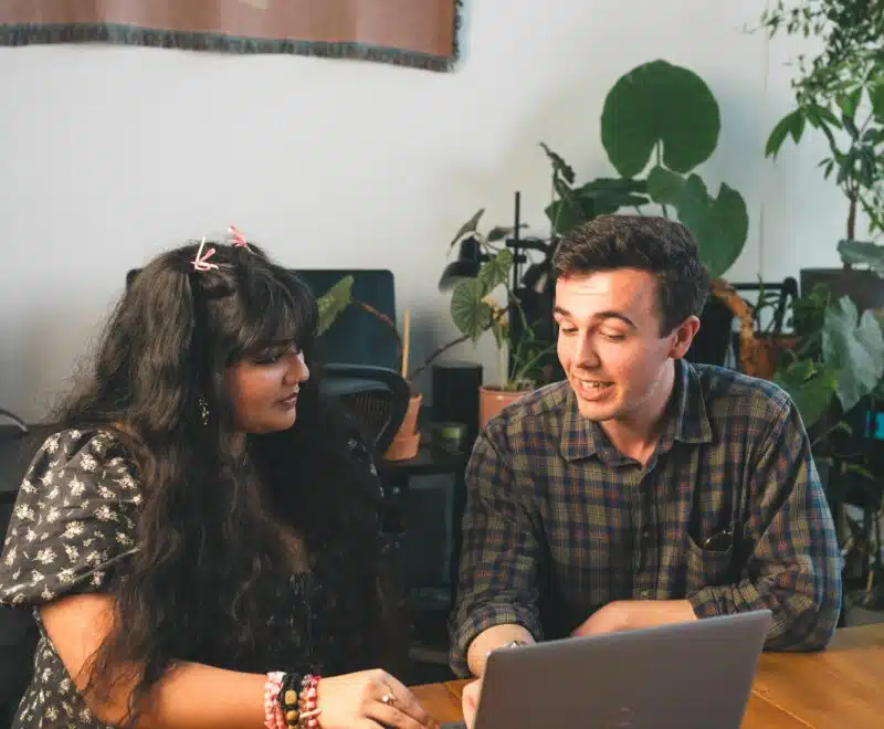 Young person talking to adult sitting in front of laptop