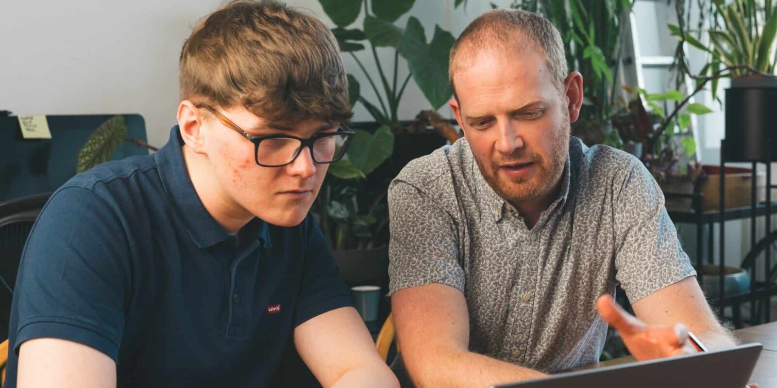 Two people looking at a laptop, sat at a desk in an office.