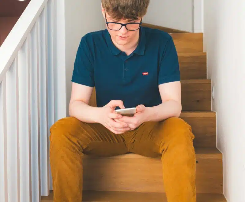 Young man sitting on stairs in a house, looking at his phone