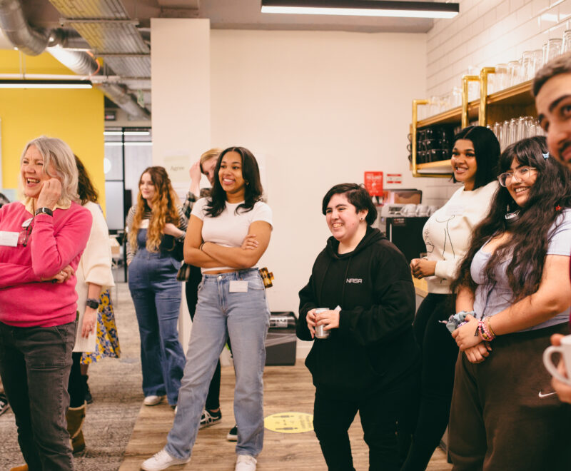 Group of staff and young people smiling watching someone speak