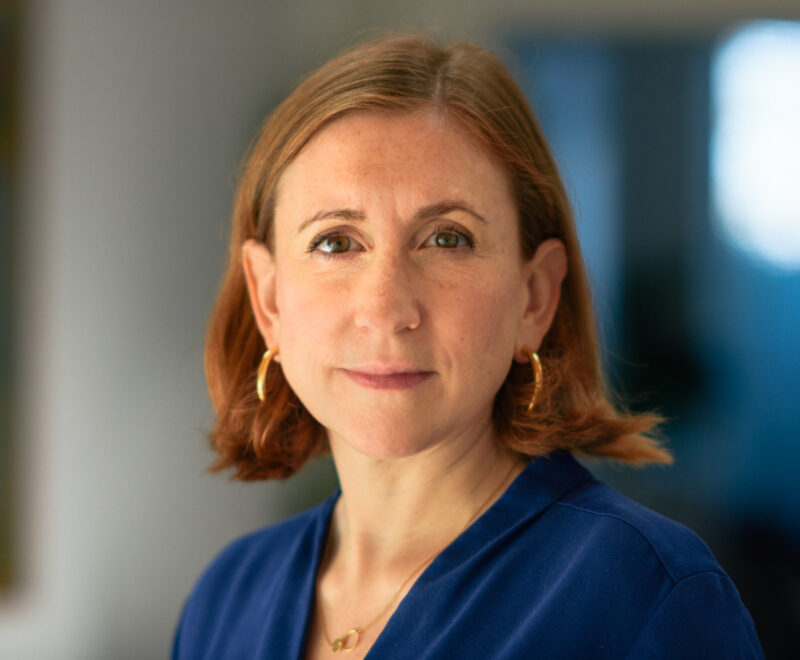 Headshot of Katharine Sacks-Jones. Katharine is wearing a blue top, gold earrings and has cropped auburn hair
